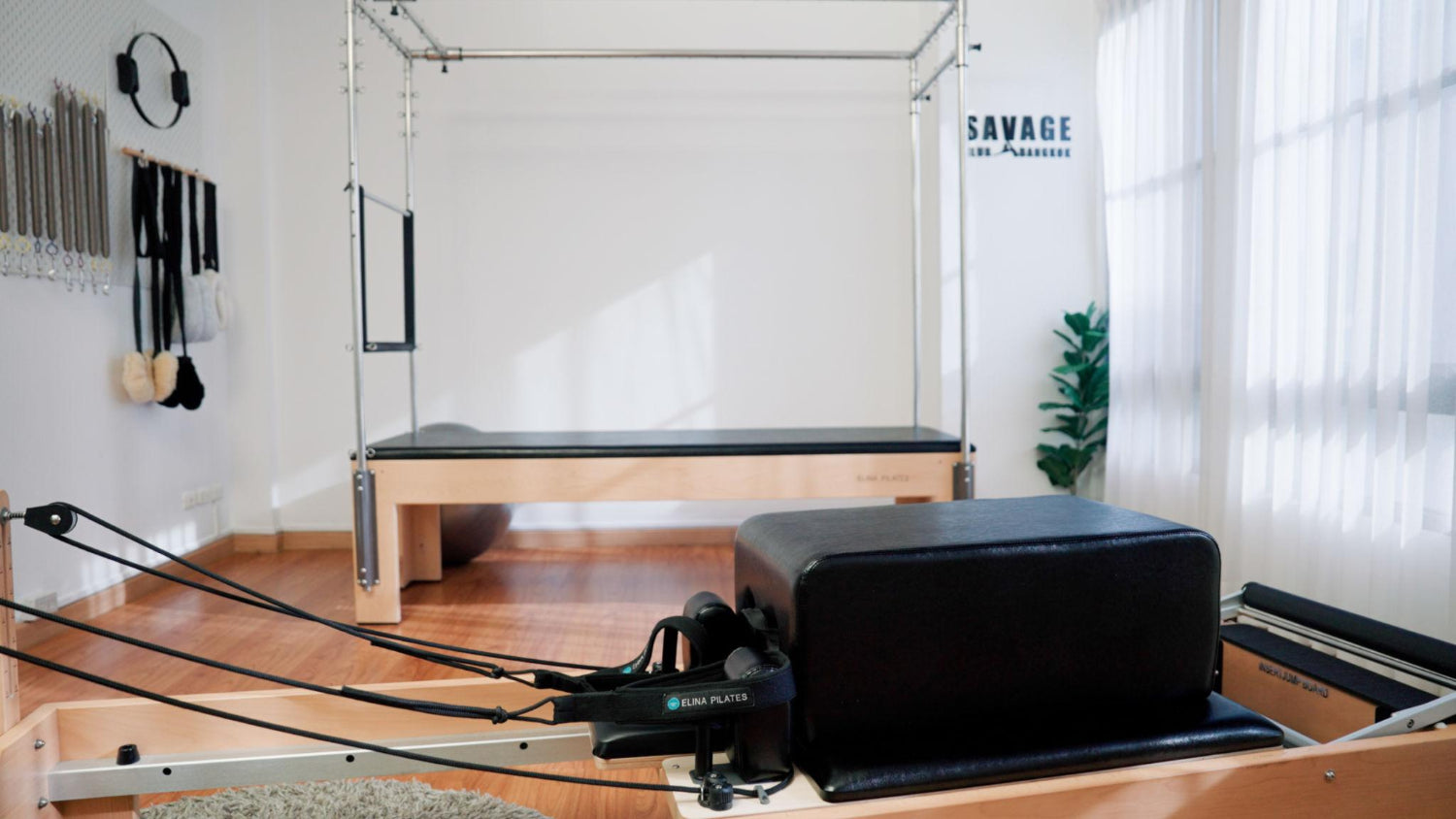 Reformer Pilates machine in a bright studio with wooden floors, natural light, and neatly organised equipment on the wall.