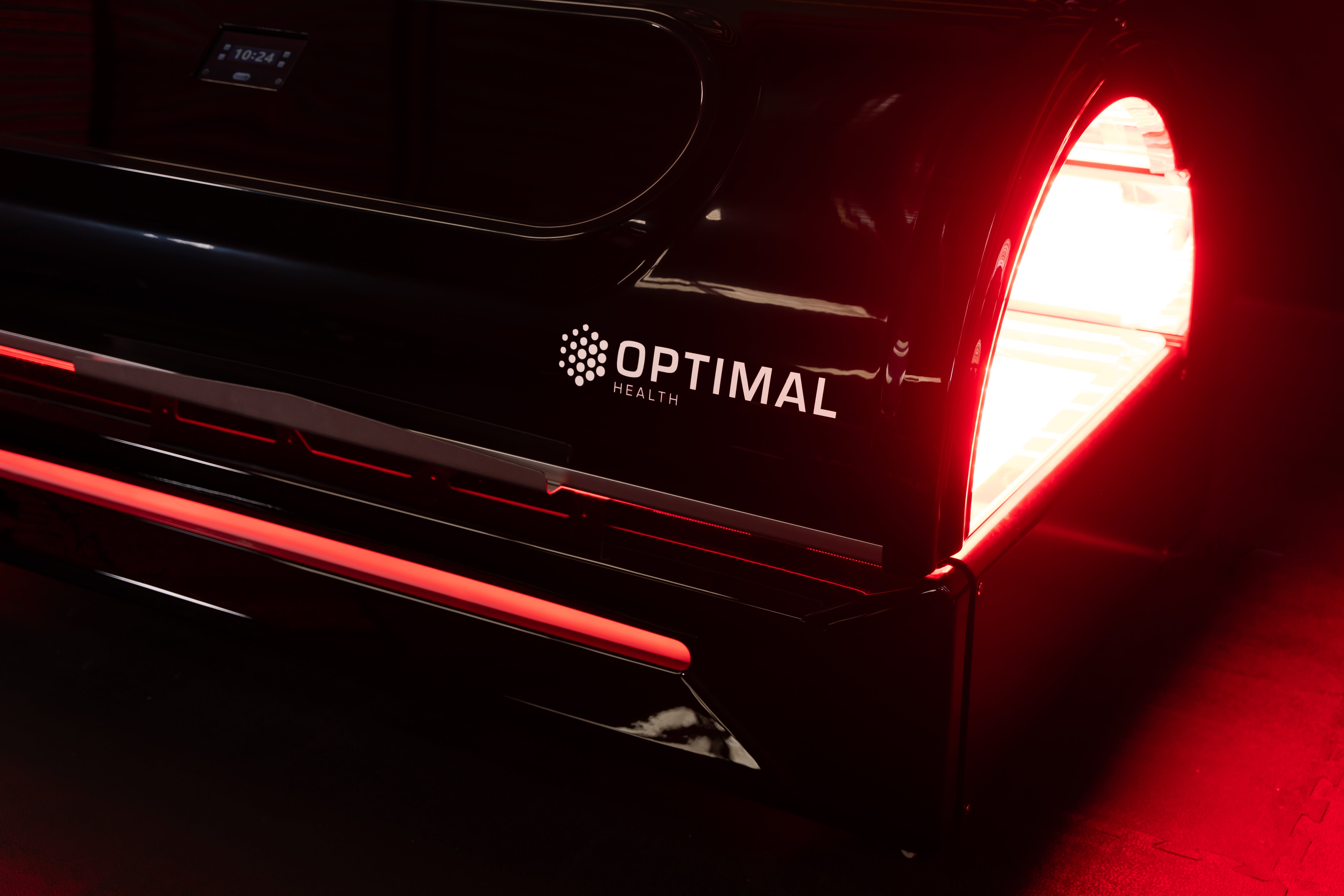 Side view of the Optimal Health red light therapy bed with logo and red LED glow.