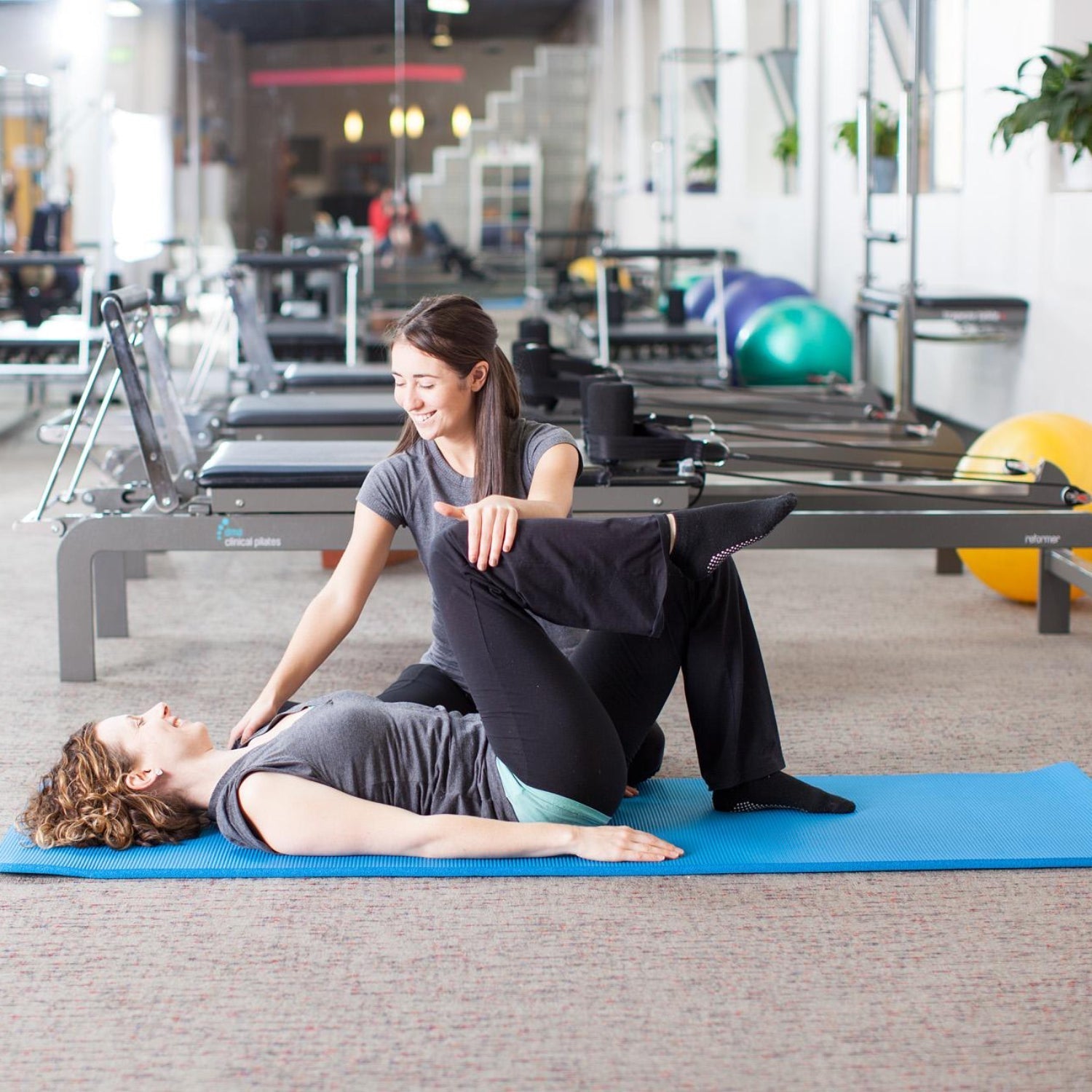 Clinical Pilates session with instructor guiding lower back rehabilitation and safe alignment on a mat