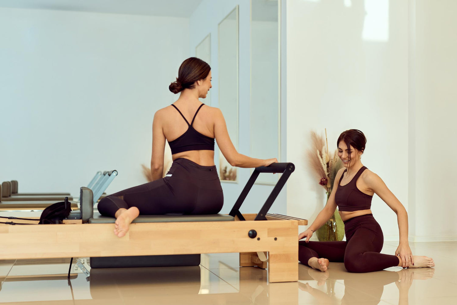 Two women practising reformer Pilates in a bright, modern studio with a calm and relaxed atmosphere