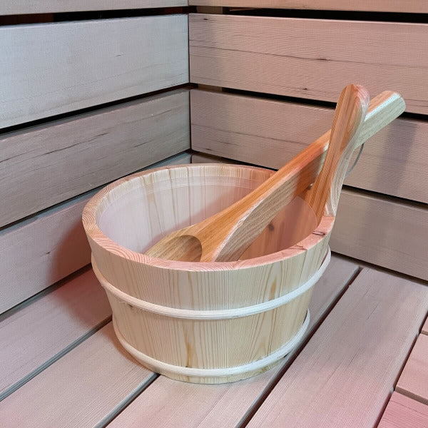 Wooden sauna bucket and ladle set placed on cedar bench inside sauna.