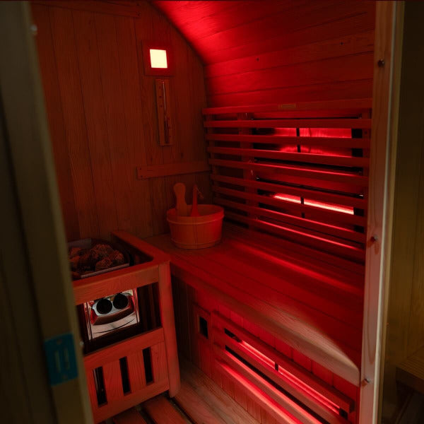 Interior of hybrid barrel sauna with red infrared lighting and wooden bucket
