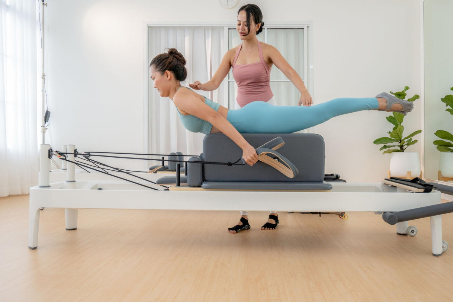 Pilates instructor guiding a client through a reformer exercise in a bright, modern studio