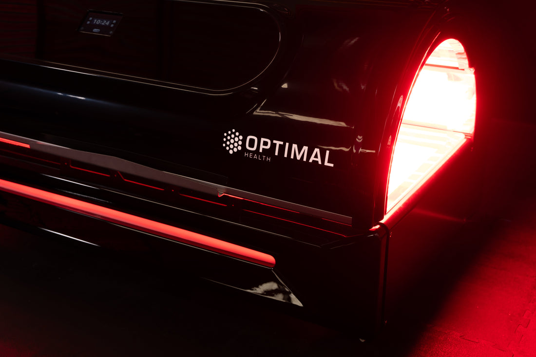 Side view of the Optimal Health red light therapy bed with logo and red LED glow.