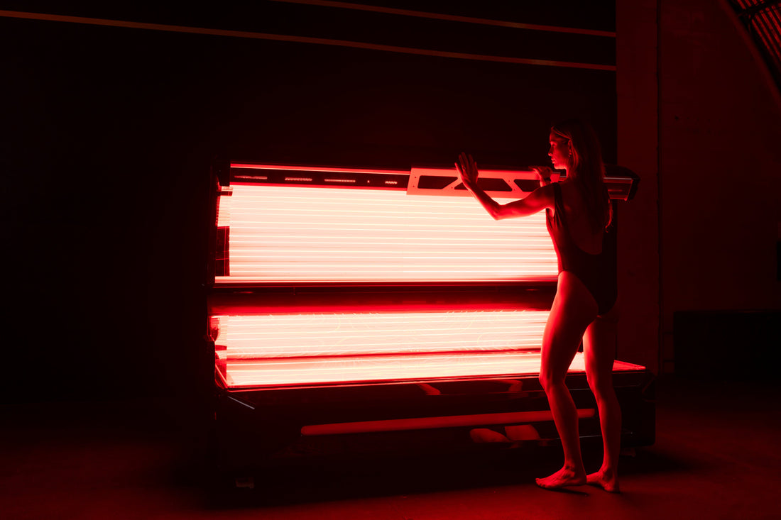 Woman opening the Optimal Health red light therapy bed in a dark studio environment.