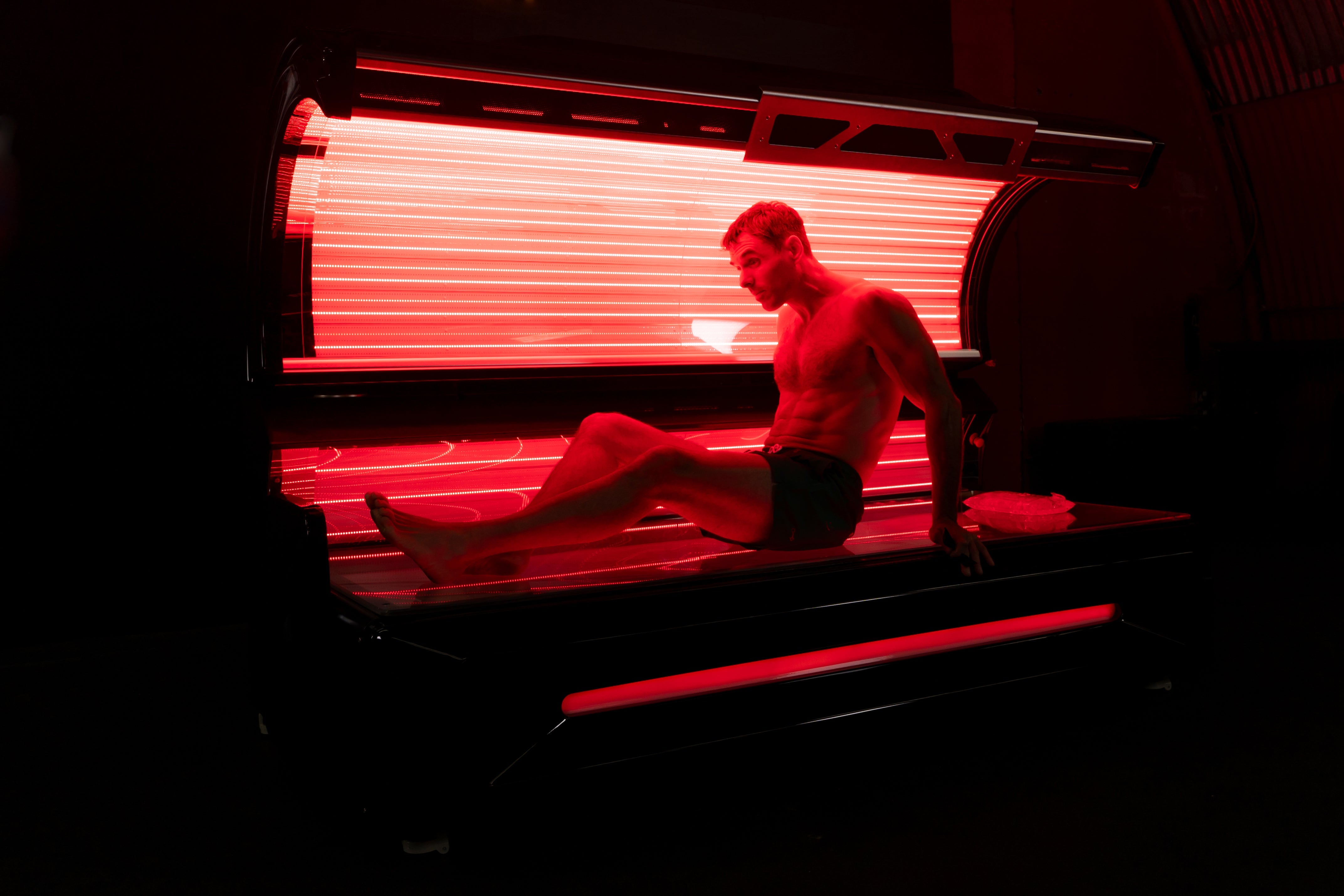 Man sitting inside the Optimal Health red light therapy bed with red LEDs illuminated.