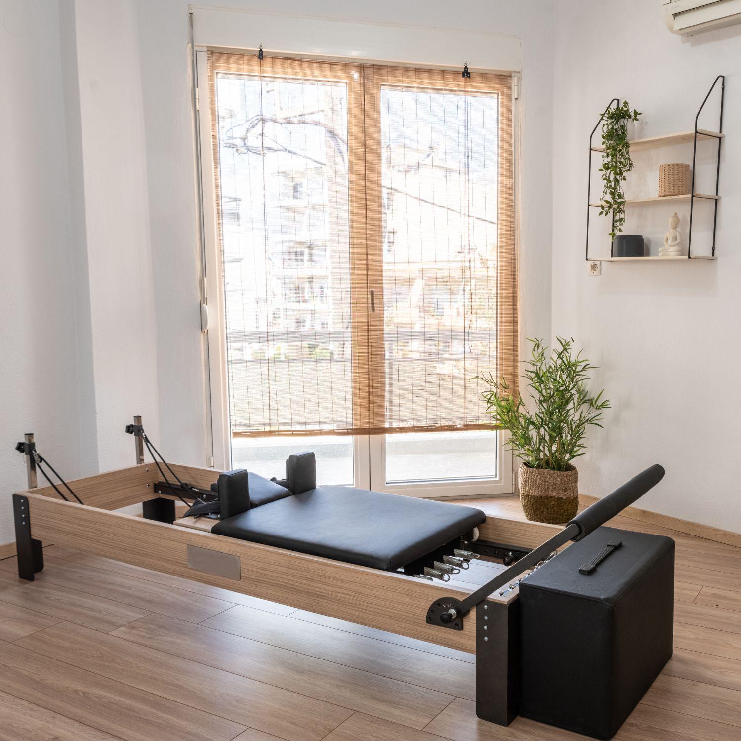 Reformer Pilates machine in a bright home studio with wooden flooring, natural light, and minimal decor
