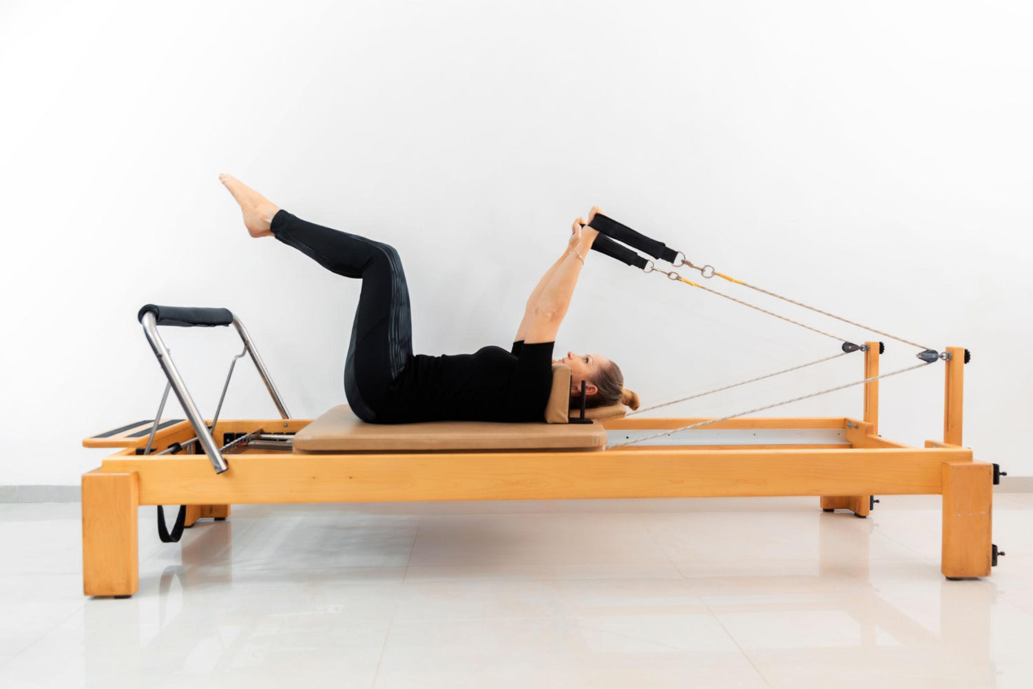 Woman performing a double leg stretch on a wooden reformer Pilates machine focusing on core strength and control