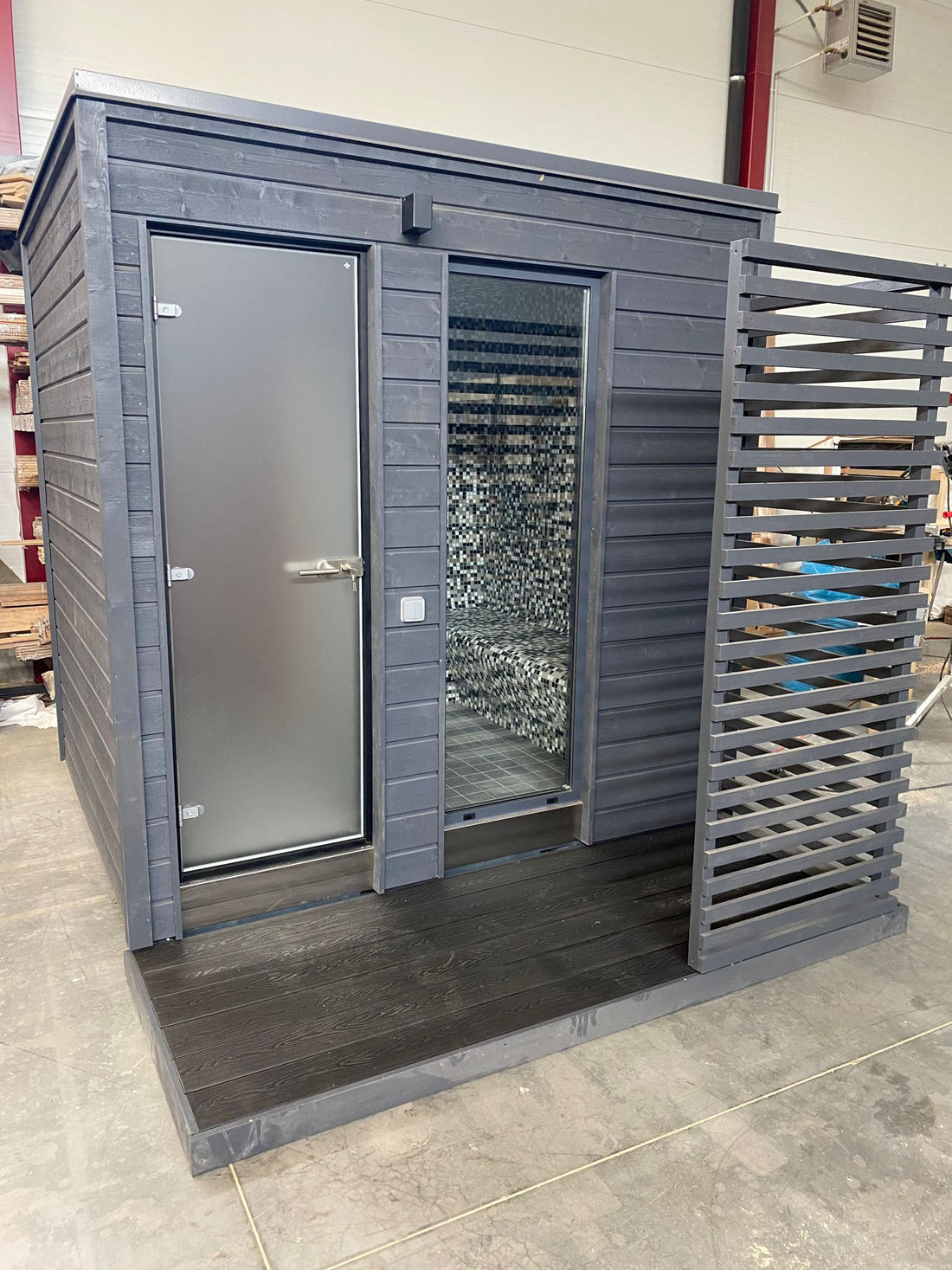 KUUT Outdoor Steam Sauna on a factory floor, showing frosted glass entry and interior mosaic tile walls.