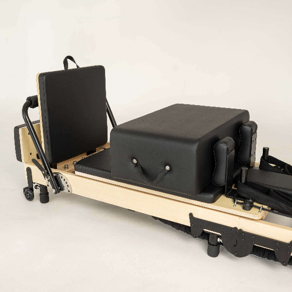 Black Pilates reformer with maple wood frame and accessories neatly arranged.