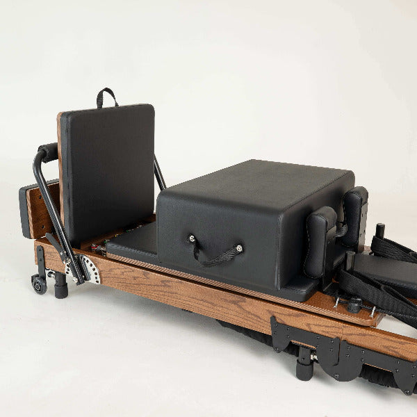Black Pilates reformer with red oak frame and accessories arranged beside it.