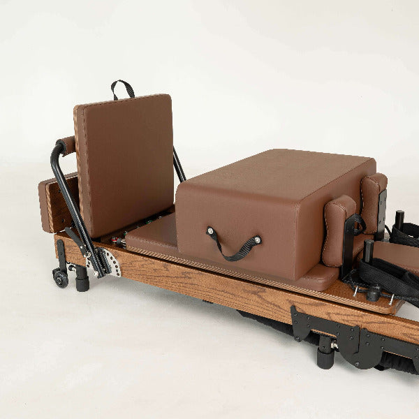 Chocolate brown Pilates reformer with red oak frame and box attachment.
