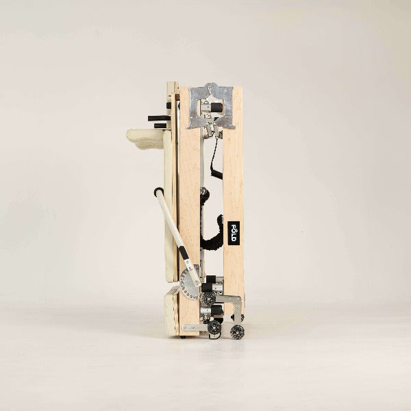 Beige Pilates reformer side view showing compact folding mechanism.