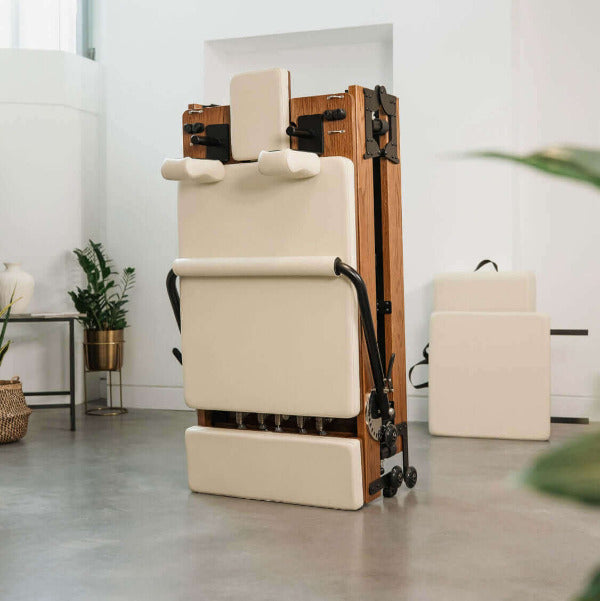 Beige foldable Pilates reformer upright with red oak wood frame in bright room.