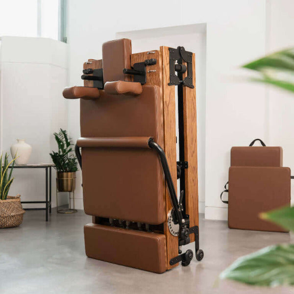 Beige foldable Pilates reformer upright with red oak wood frame in bright room.