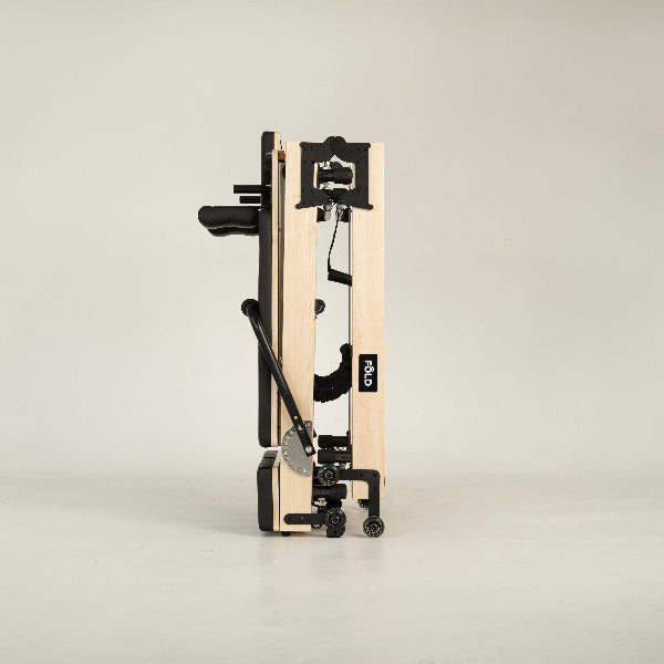 Black Pilates reformer side profile with folded design and maple frame.