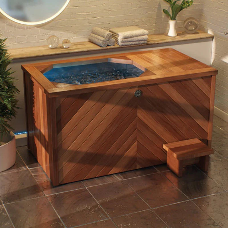 Brass Monkey Ice Bath with a premium wooden exterior and step stool, placed in a tiled indoor bathroom with ambient lighting and decor.