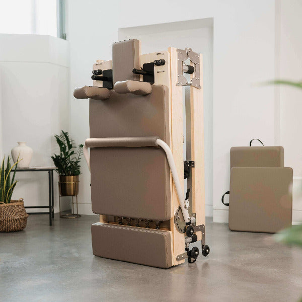 Mocha foldable Pilates reformer upright with maple wood frame.