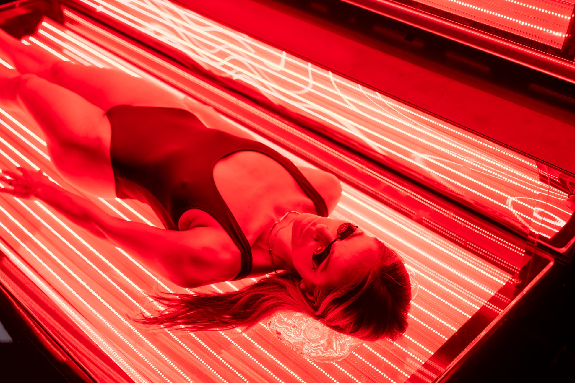 Close-up of woman lying inside the Optimal Health red light therapy bed wearing protective goggles.