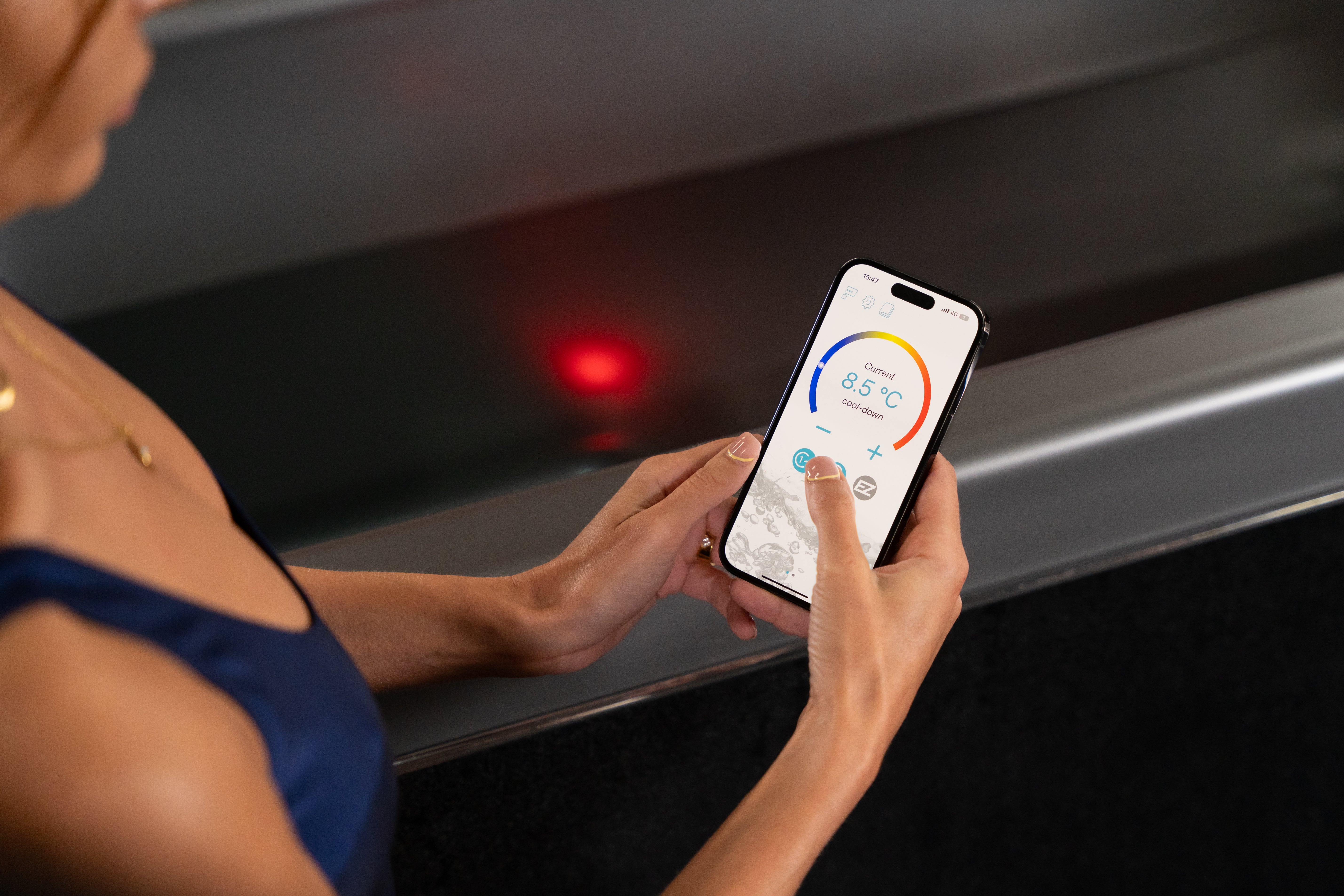 Woman adjusting temperature on smartphone next to Optimal Health Ice Bath.