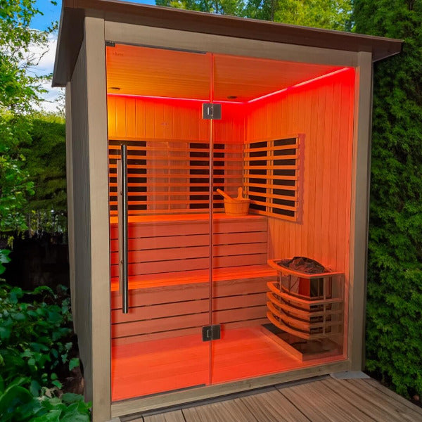 Outdoor sauna with glass front illuminated by red chromatherapy lighting.