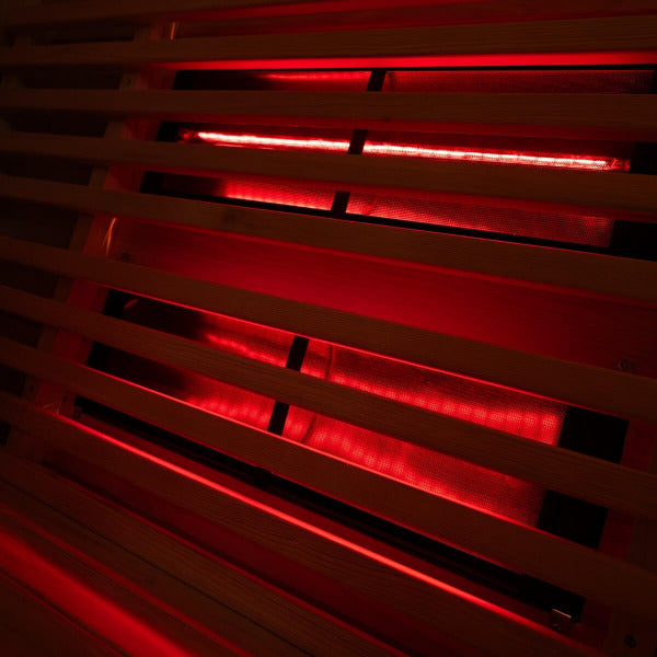Red infrared heating panels behind wooden slats inside hybrid barrel sauna