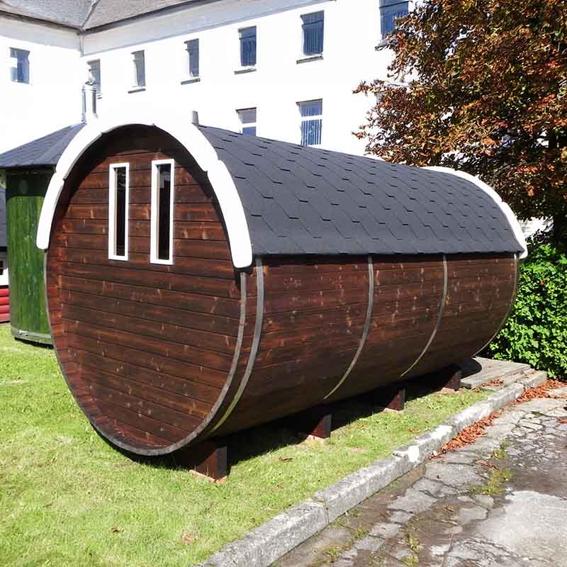 Rear view of a dark wood barrel sauna with black shingle roof outdoors.
