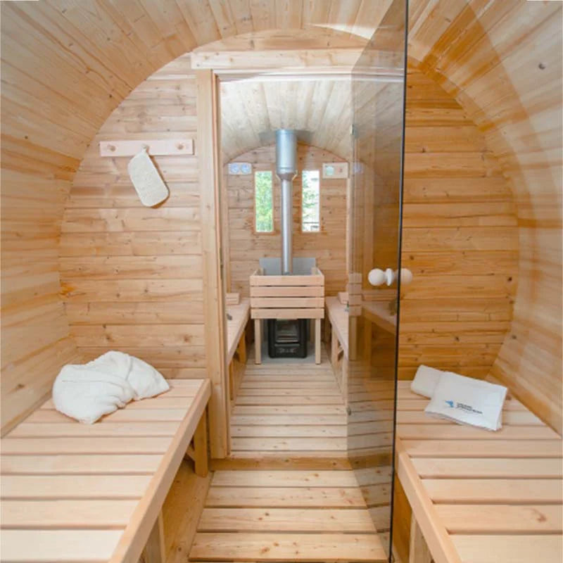 Wooden barrel sauna interior with benches and glass door separating heater area.