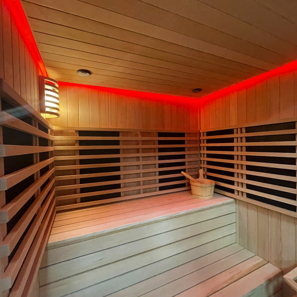 Red chromatherapy lighting inside wooden sauna with bucket and ladle on bench